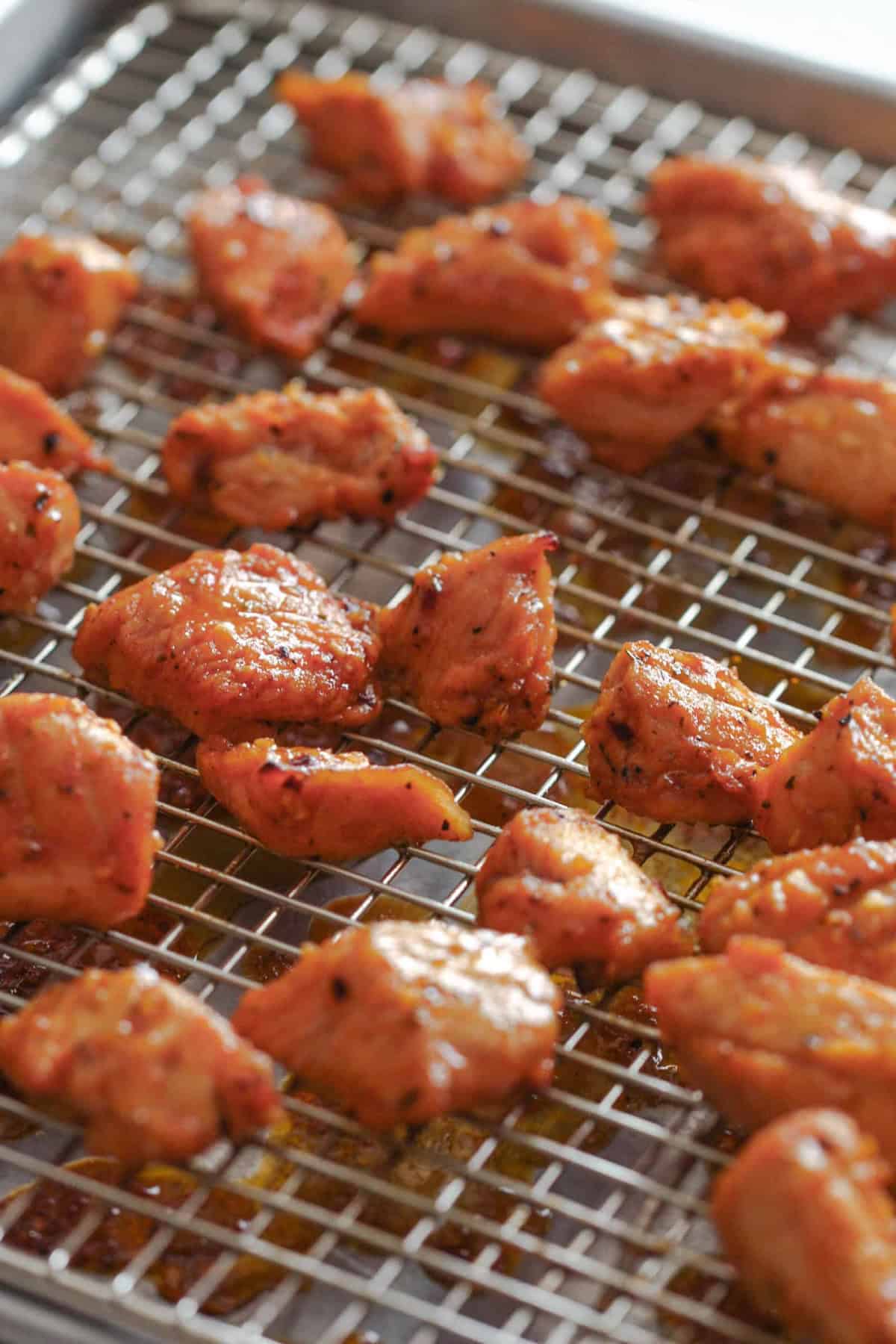 Chunks of seasoned chicken pieces arranged on a wire rack over a baking sheet.