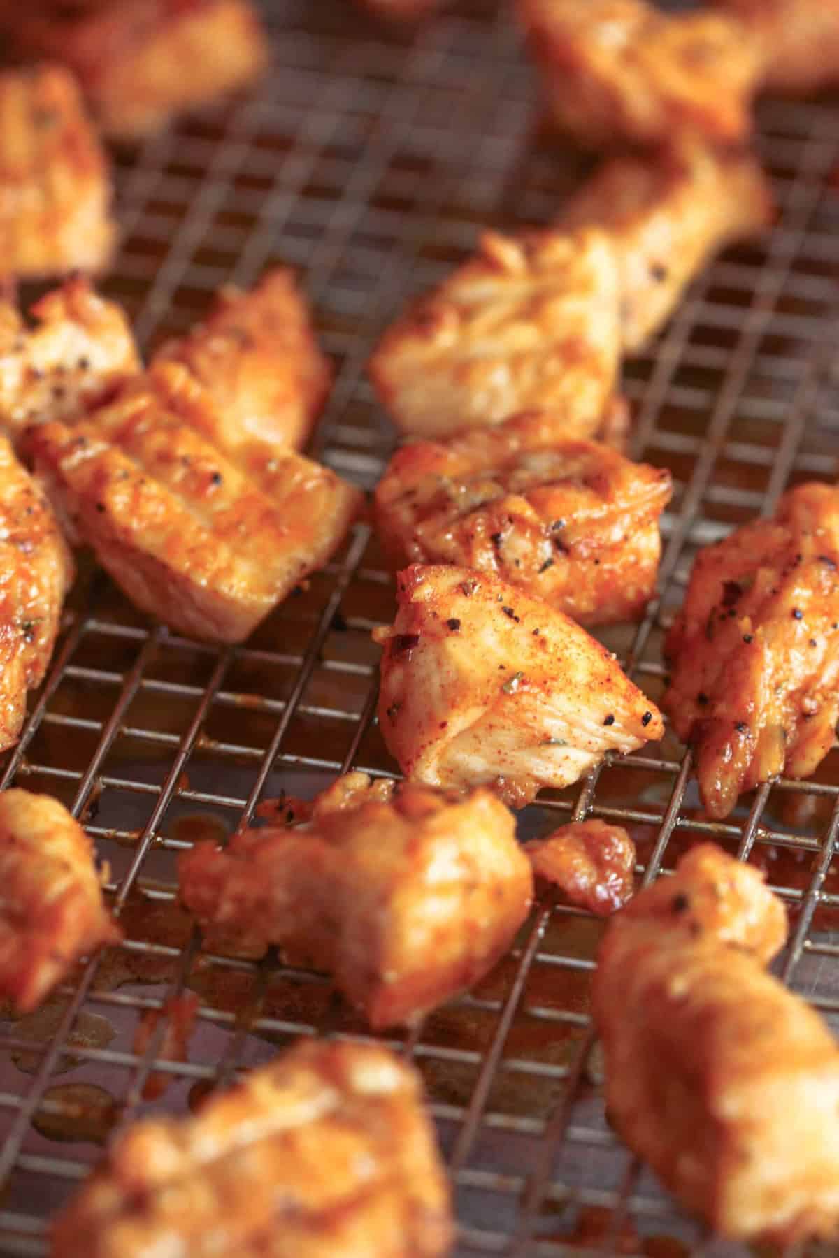 Cooked pieces of seasoned chicken on a wire rack.