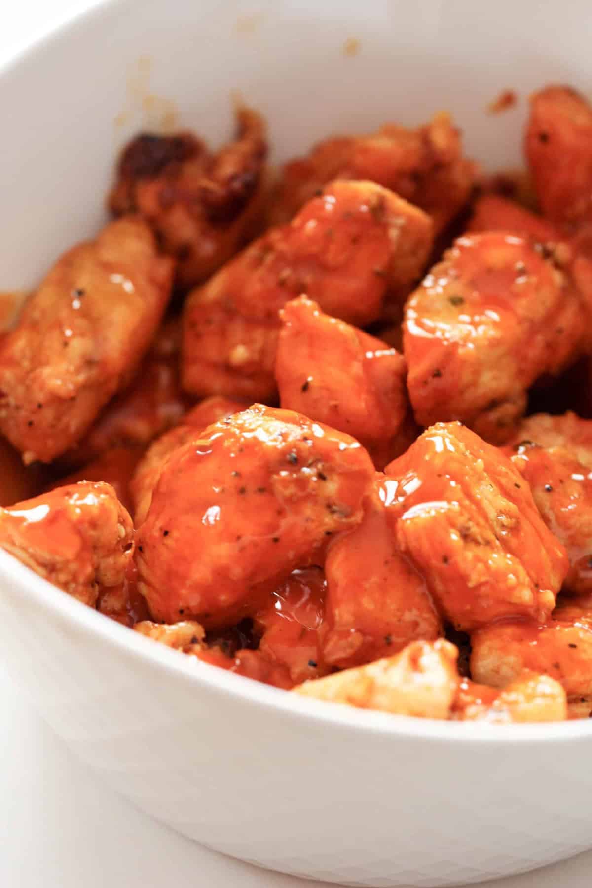 A bowl filled with cooked chicken pieces coated in a red sauce.