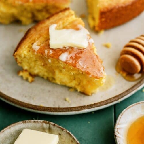 3 slices of cornbread on a plate topped with a pat of butter and honey.