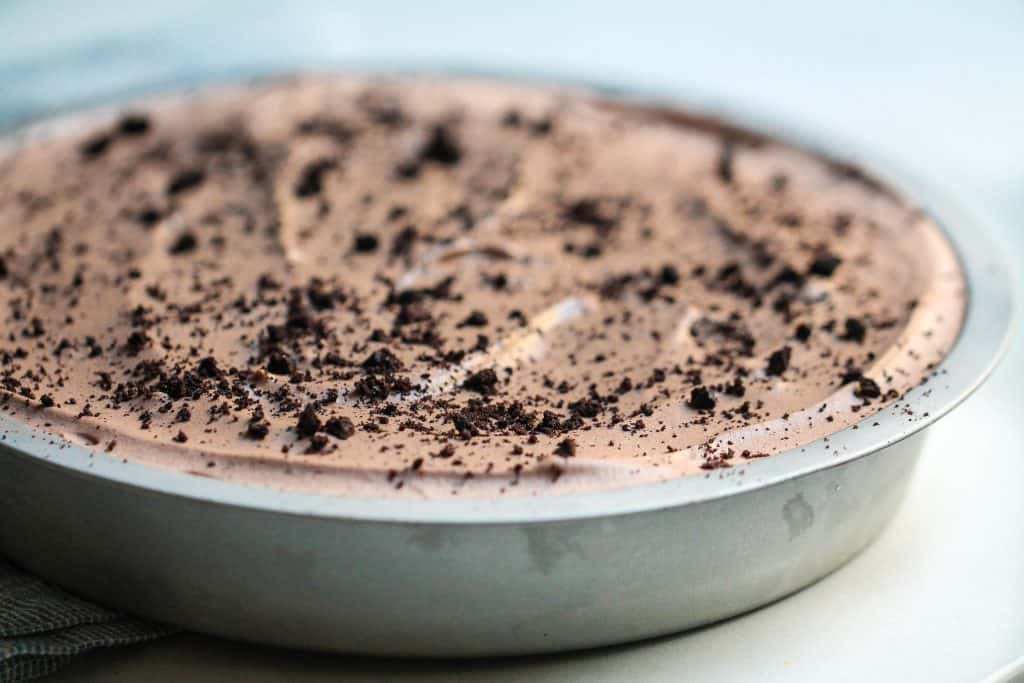 A close-up of a chocolate oreo pie topped with crumbled bits in a round metal pan on a light background.