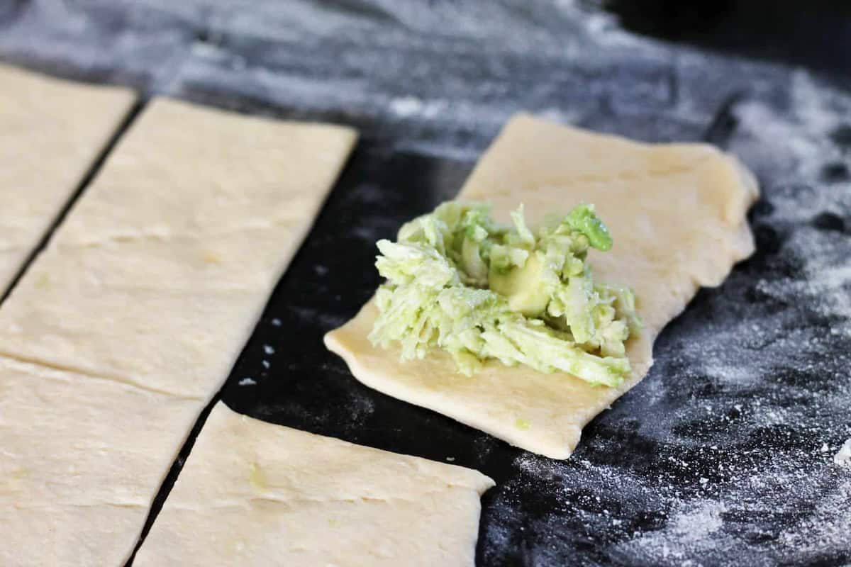 Dough rectangles on a floured surface, one topped with a mixture of shredded cheese and avocado.