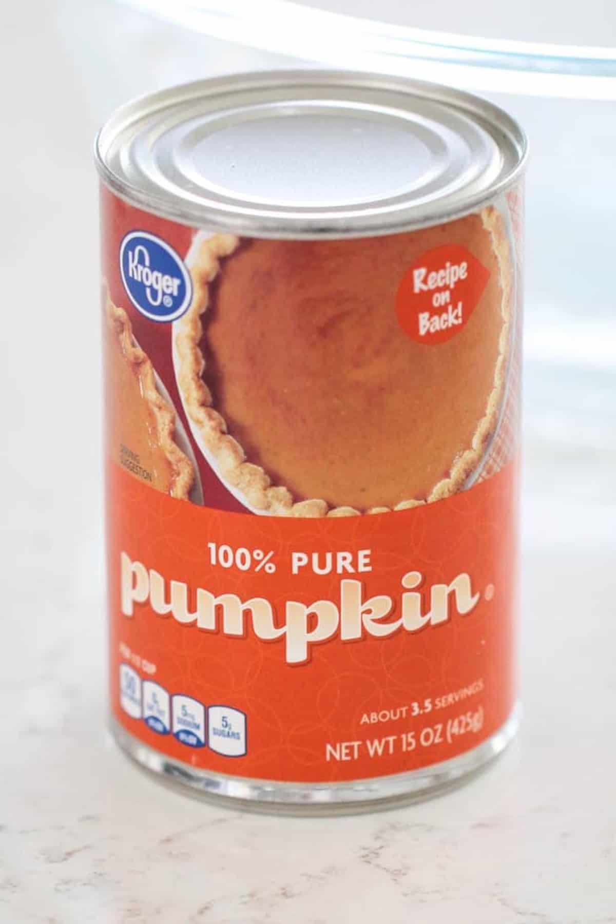 A can of Kroger 100% pure pumpkin, net weight 15 oz, with an image of pumpkin pie and a note indicating a recipe on the back.