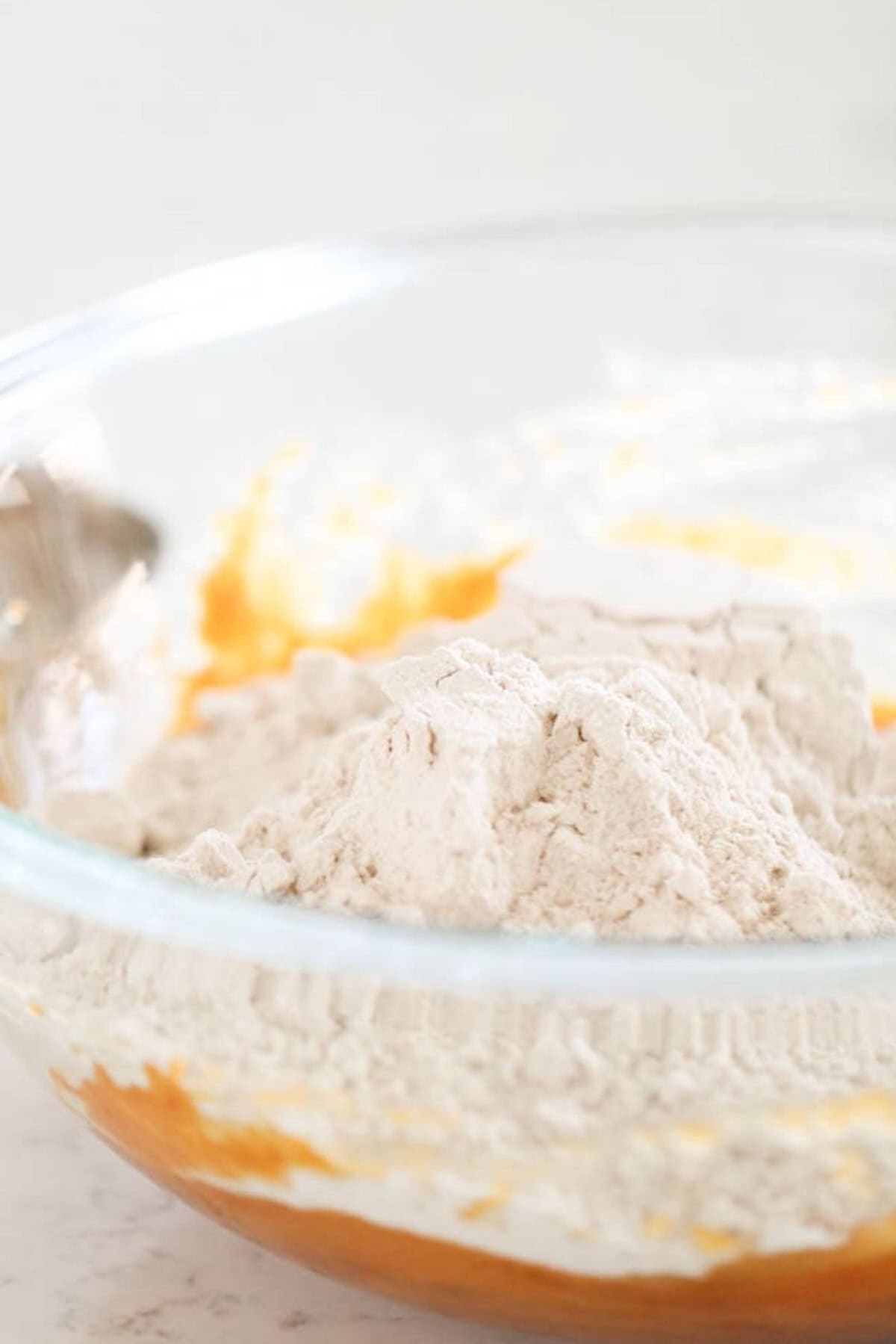 A glass bowl containing a mixture of white flour and an orange substance, which appears to be in the process of being combined.