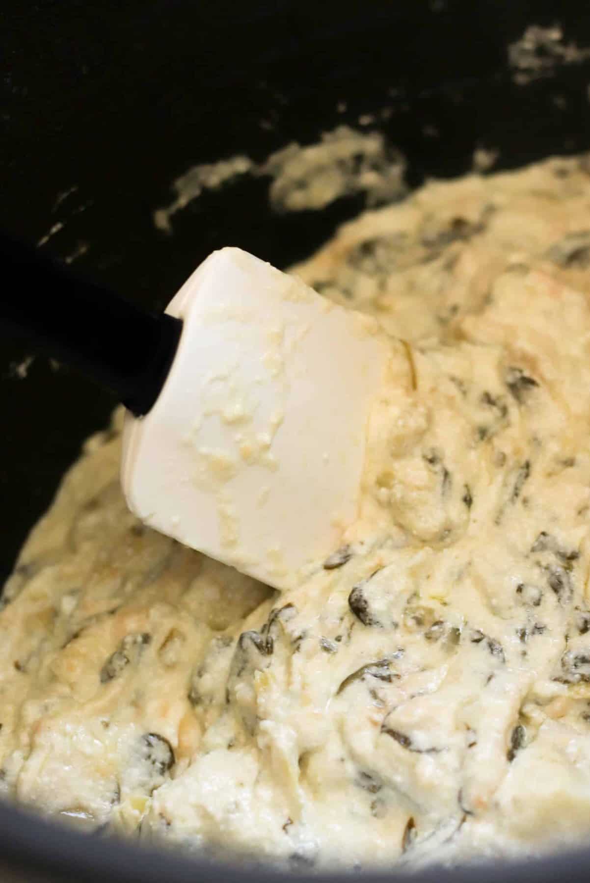 Close-up of creamy spinach and artichoke dip being stirred with a white spatula.