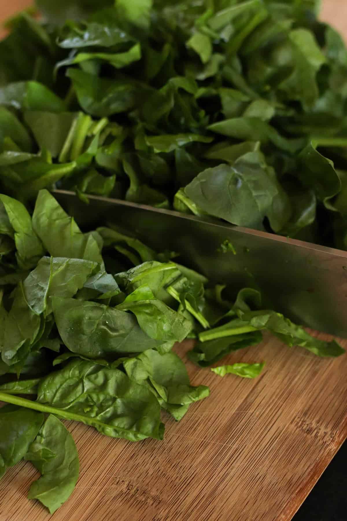 Chopped green leafy spinach on a wooden cutting board with a knife.