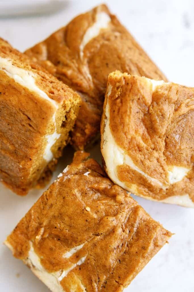 Close-up of four pumpkin cheesecake bars with a marbled swirl pattern on top, placed on a white surface.