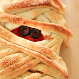 A loaf of bread resembling a mummy, with twisted dough forming bandages and black olives and red sauce simulating eyes and a mouth.