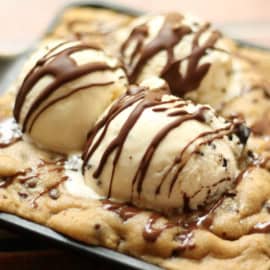 Three scoops of vanilla ice cream with chocolate drizzle sit on a baked cookie.