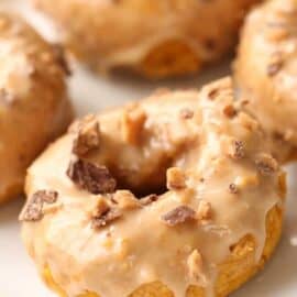 A close-up of glazed doughnuts topped with chunks of chocolate on a white surface.