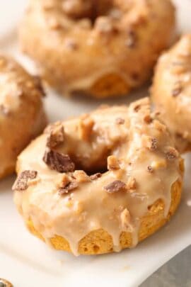 A close-up of glazed doughnuts topped with chunks of chocolate on a white surface.