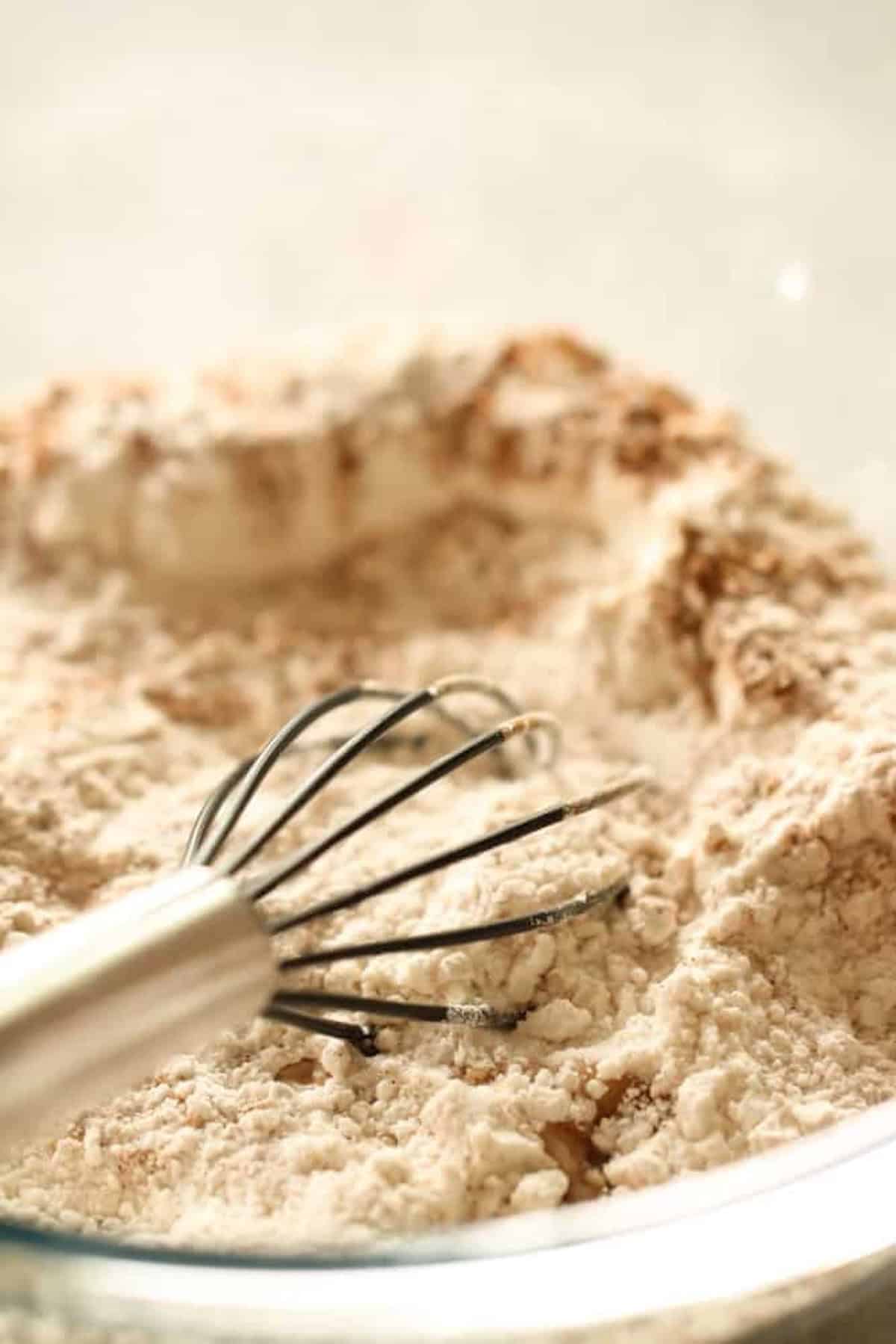 A metal whisk resting in a bowl of flour.