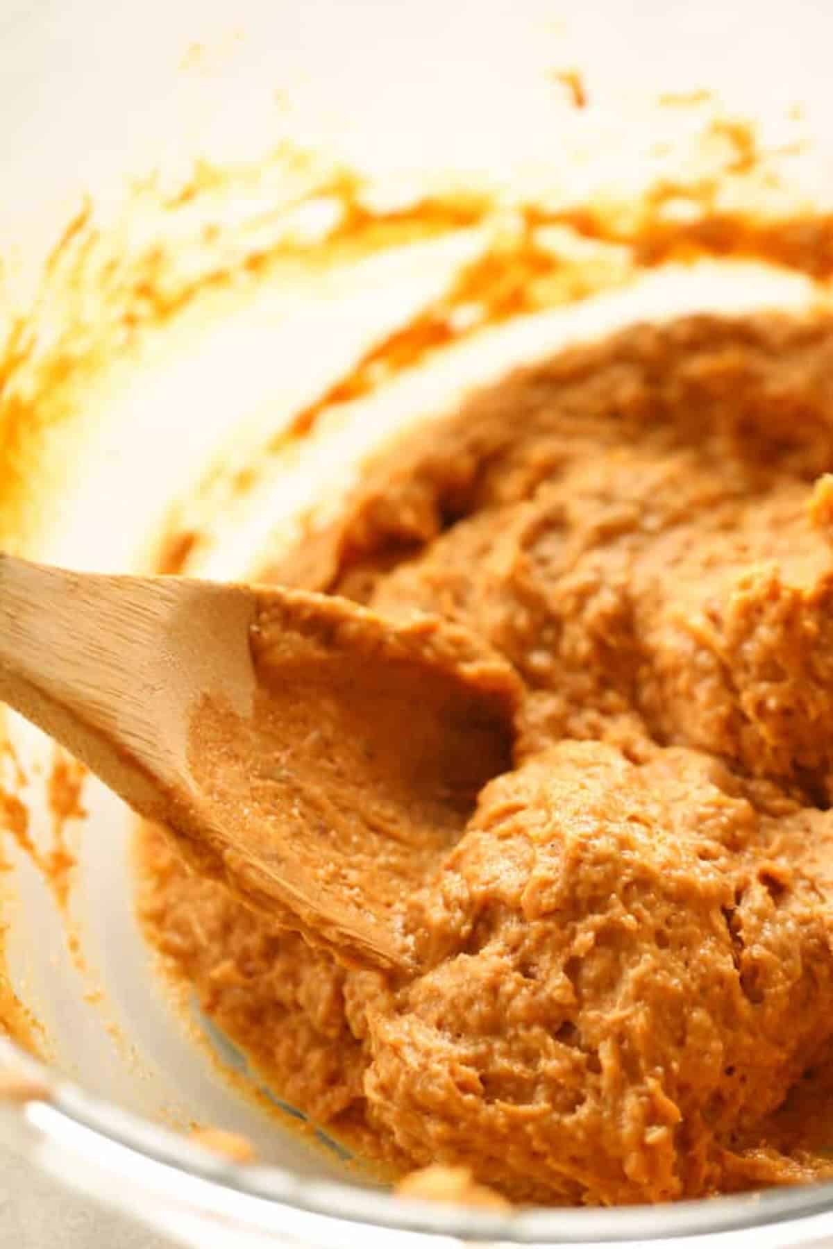 A wooden spoon stirring a thick, brown dough-like mixture in a bowl.