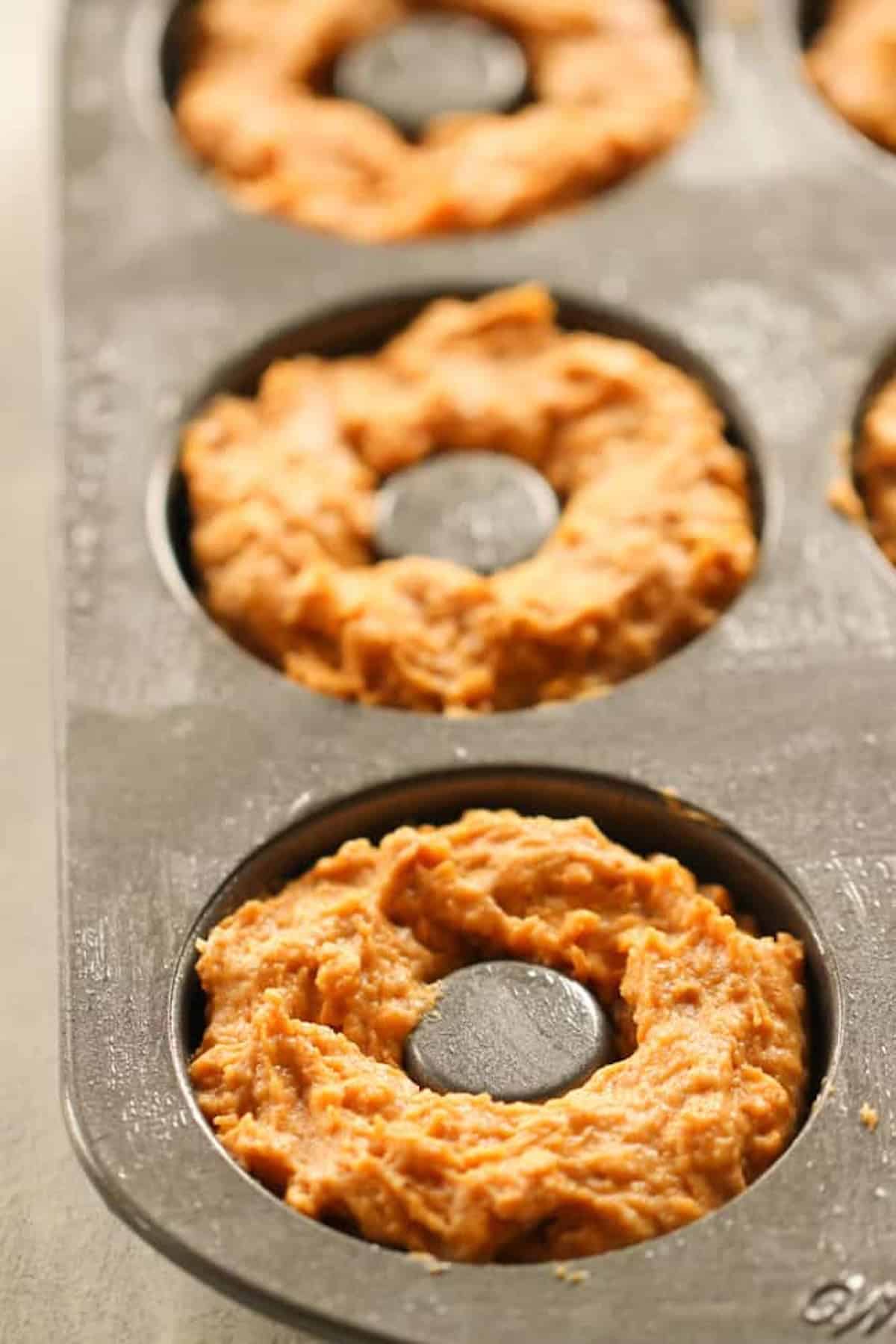 Close-up of a muffin pan with doughnut-shaped batter evenly distributed in each cavity, ready for baking.