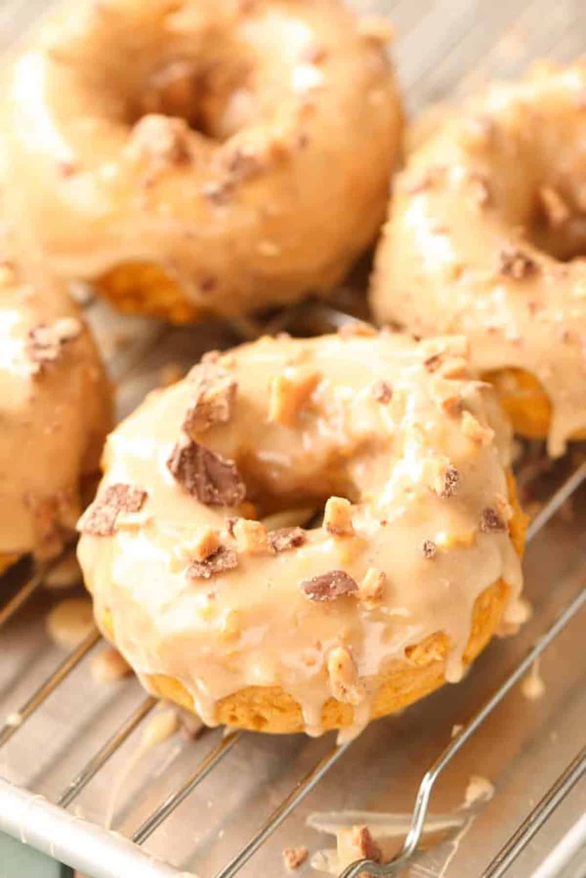 Close-up of four glazed donuts with crushed toppings resting on a wire rack.