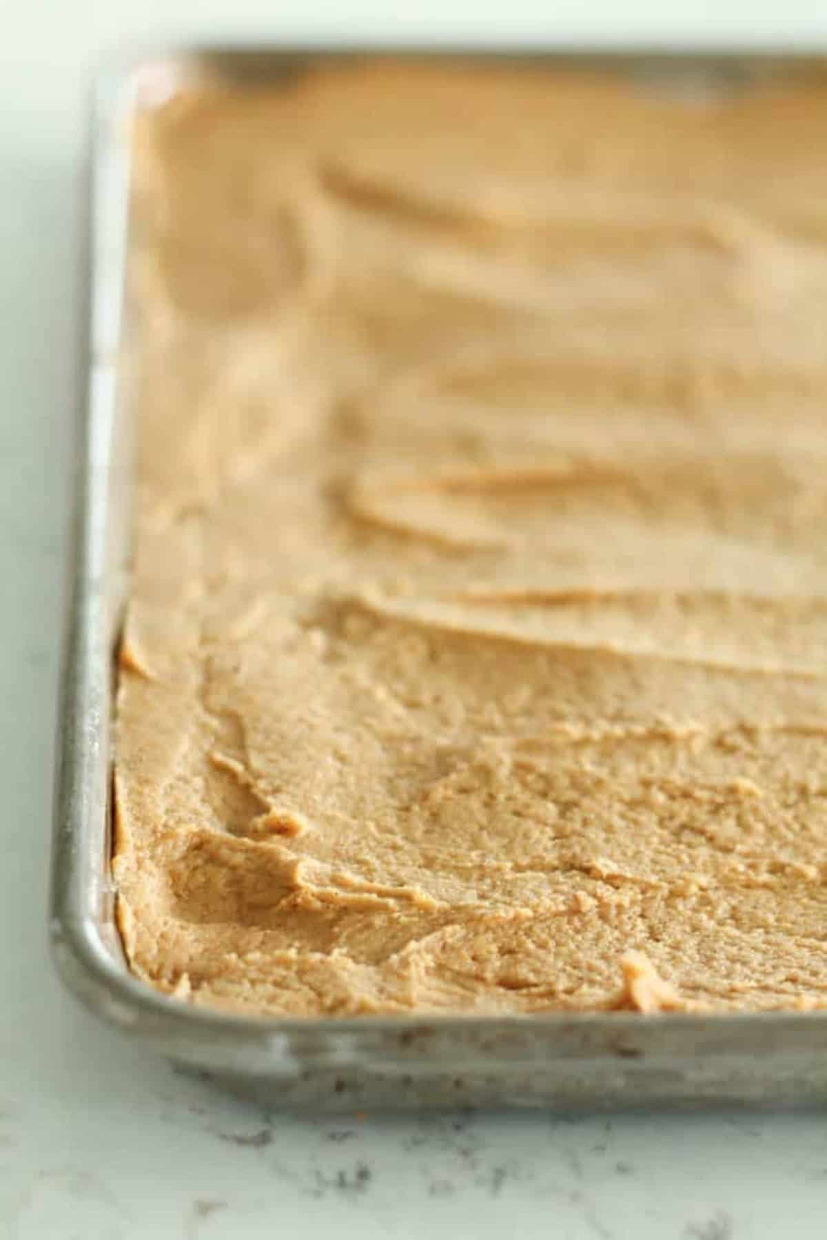 A baking pan filled with evenly spread pumpkin sugar cookie batter.