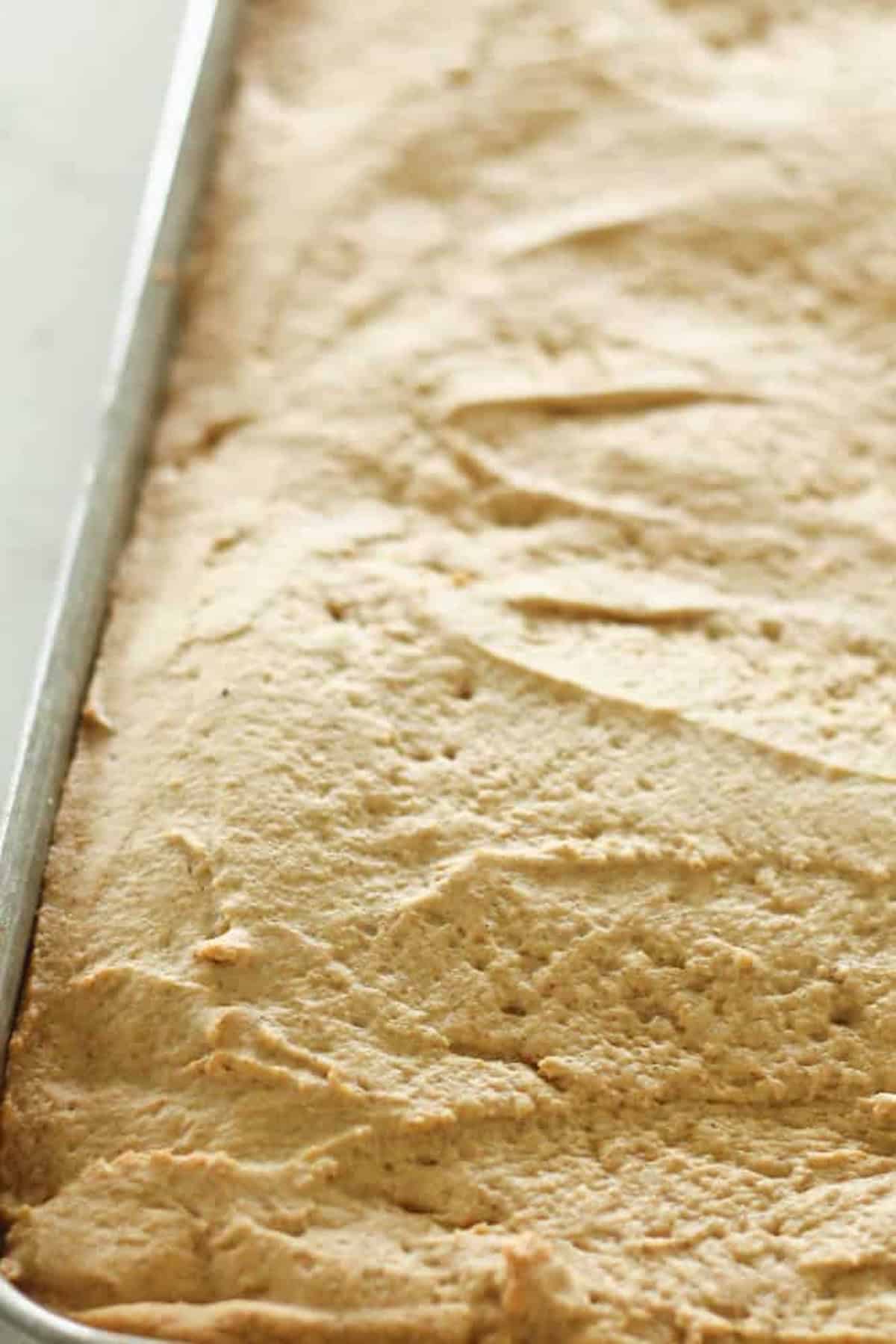 A close-up of a large rectangular baking tray filled with evenly spread baked batter, with a light golden-brown crust on the surface.