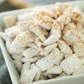 A white bowl filled with powdered sugar-coated snack pieces, possibly resembling a type of dessert or sweet treat.