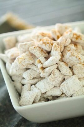 A white bowl filled with powdered sugar-coated snack pieces, possibly resembling a type of dessert or sweet treat.