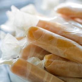 Homemade Microwave Caramels wrapped individually in pieces of wax paper and in a bowl.