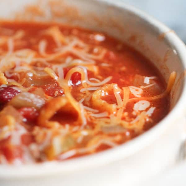 A close-up shot of a bowl filled with tomato-based soup, topped with grated cheese and chunks of vegetables.