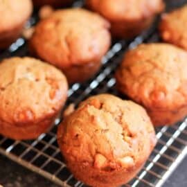 A cooling rack with several freshly baked muffins with a golden-brown top, resting on a dark surface.