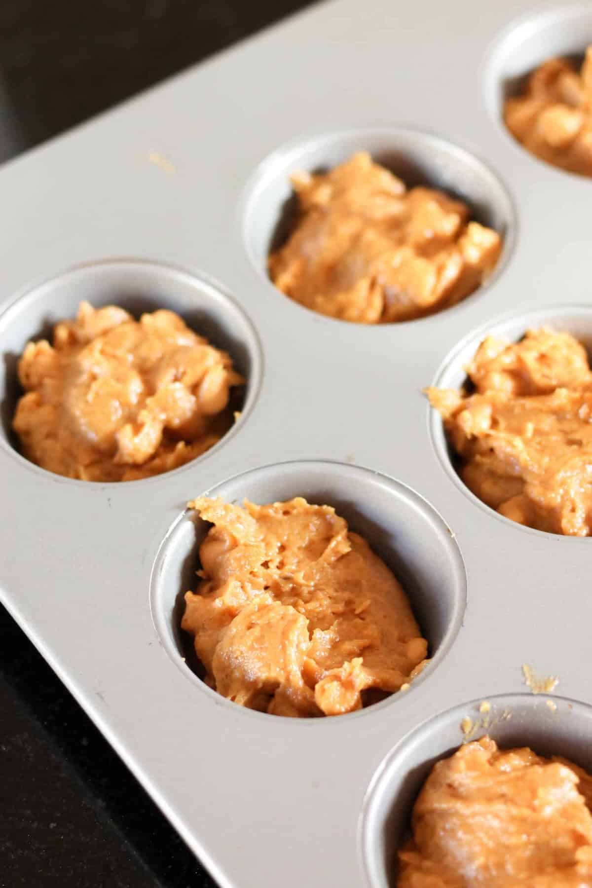 Muffin pan with six cavities filled with raw batter, ready to bake.