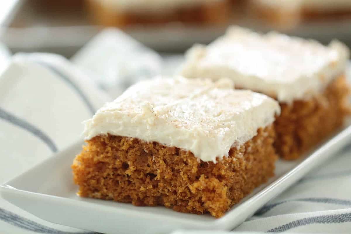 Two pieces of frosted carrot cake with a white layer of icing on top, placed on a white plate.