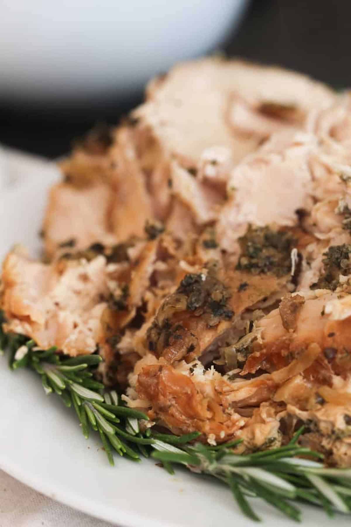 Close-up of sliced roasted turkey on a plate, garnished with fresh rosemary sprigs.