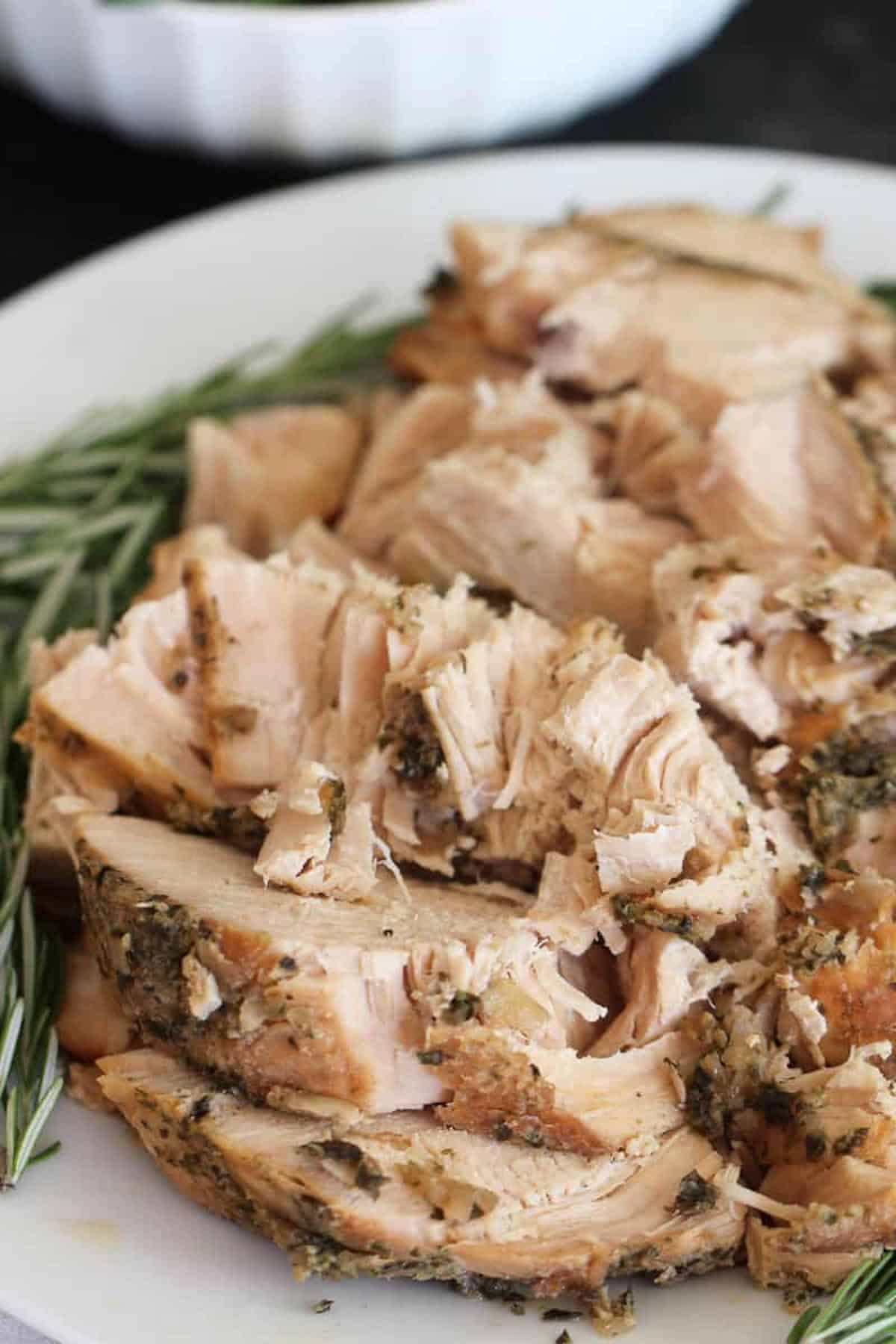 A plate of sliced, seasoned cooked turkey garnished with fresh rosemary sprigs.