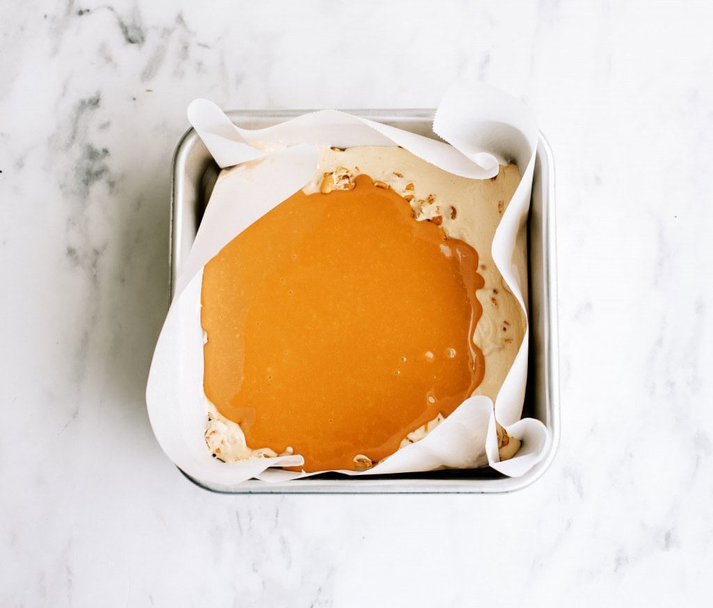 Caramel layer spread over marshmallow peanut layer in square pan.