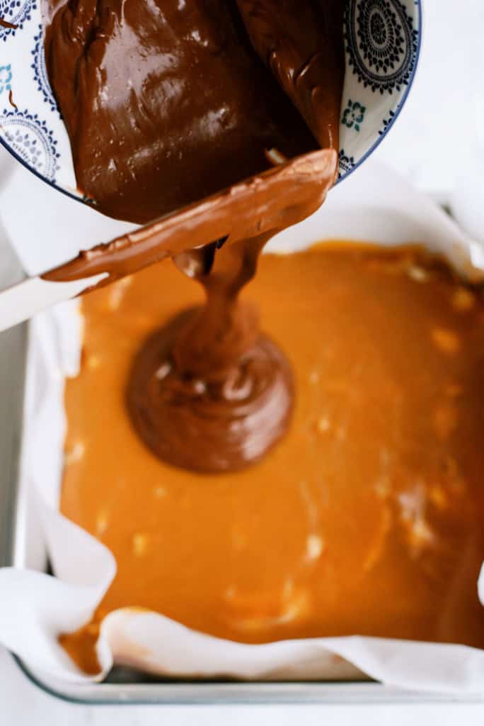 Pouring melted chocolate on top of caramel layer in square pan.