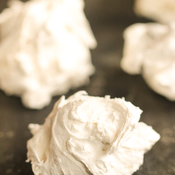 Close-up of several white meringue cookies on a dark surface.