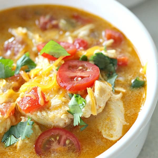 A bowl of soup containing pieces of chicken, slices of tomato, shredded cheese, and garnished with cilantro.