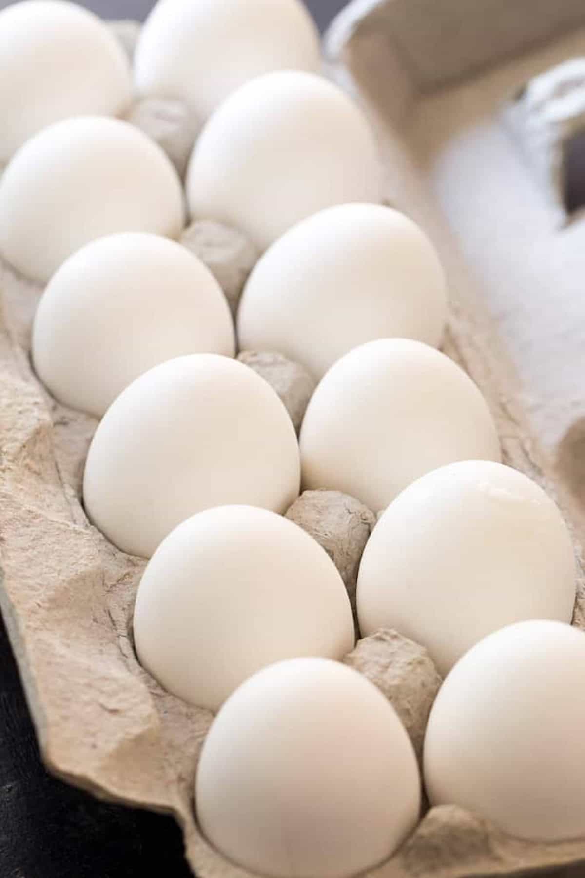 A dozen white eggs in a cardboard carton.