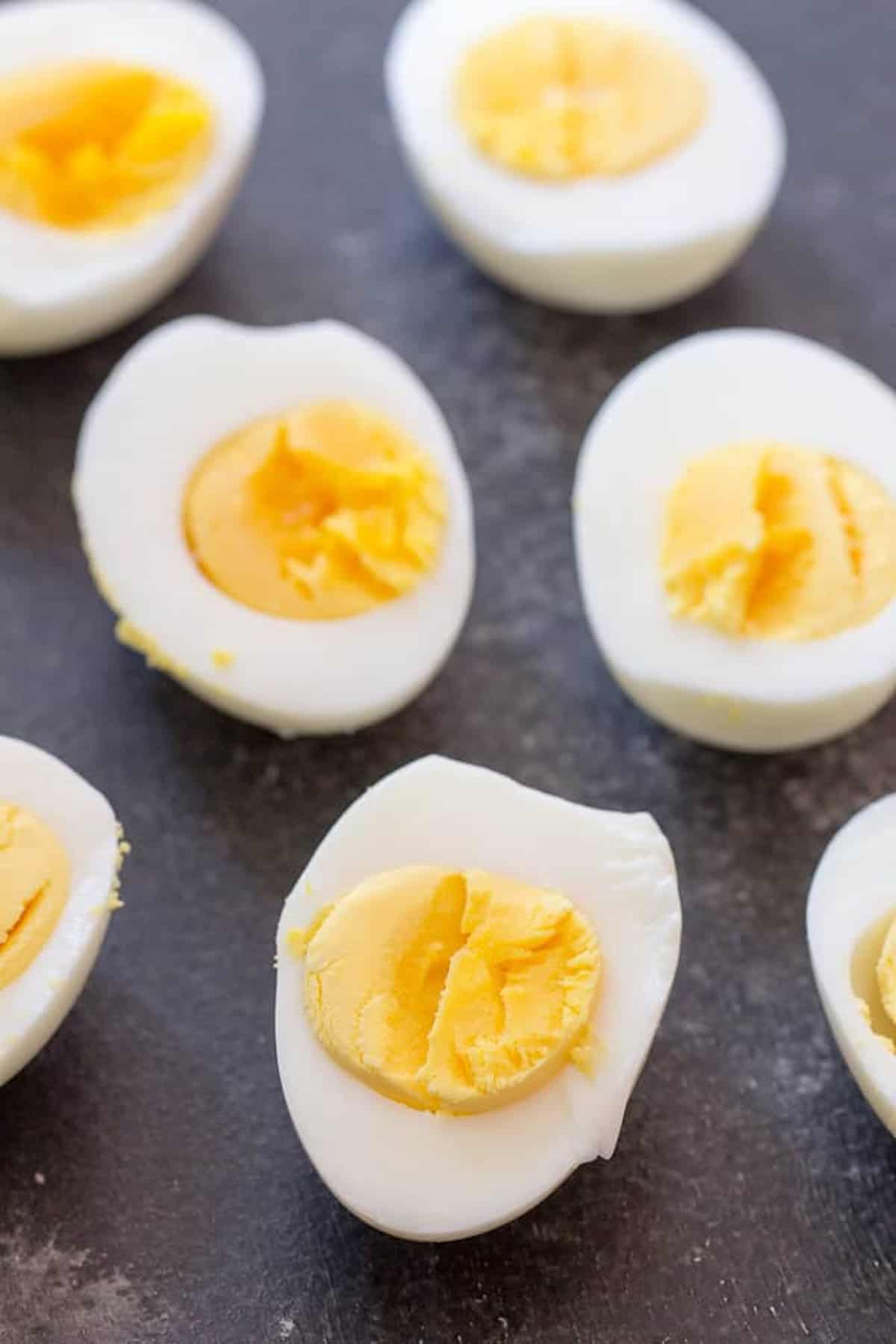 Halved hard-boiled eggs arranged on a dark surface, displaying yellow yolks and white edges.