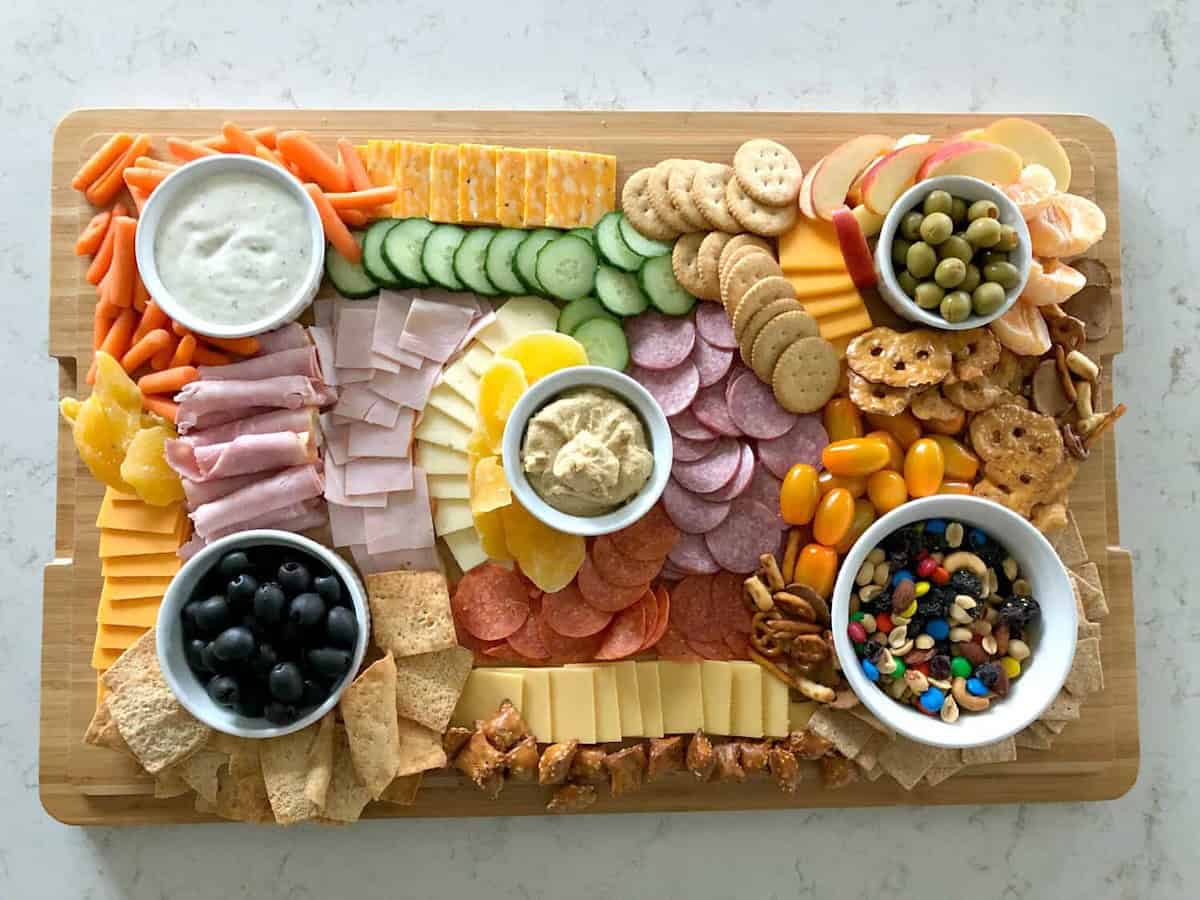 A charcuterie board with various meats, cheeses, crackers, fruits, nuts, and bowls of dips, olives, and candies.