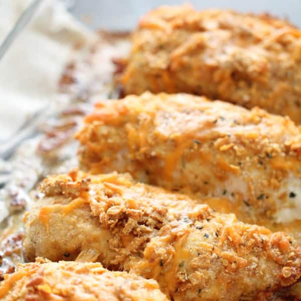 Close-up view of a glass baking dish containing four breaded and baked chicken breasts, with a golden-brown crust.