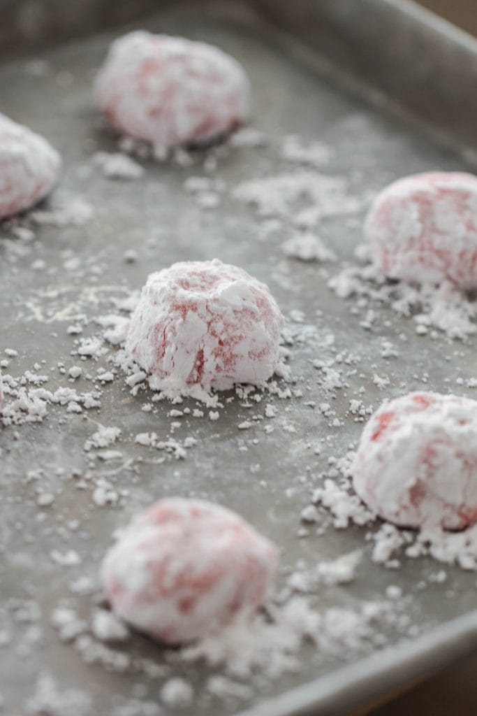 Strawberry cookie dough balls rolled in powdered sugar placed on a baking sheet.