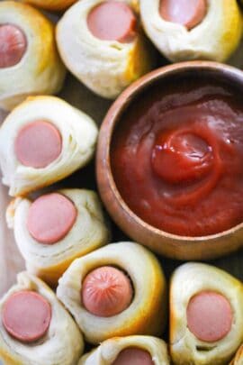 Pigs in a blanket encircle a bowl of thick, red ketchup.