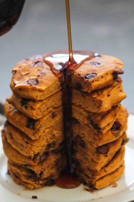 A stack of thick pancakes with visible chocolate chips being drizzled with syrup.