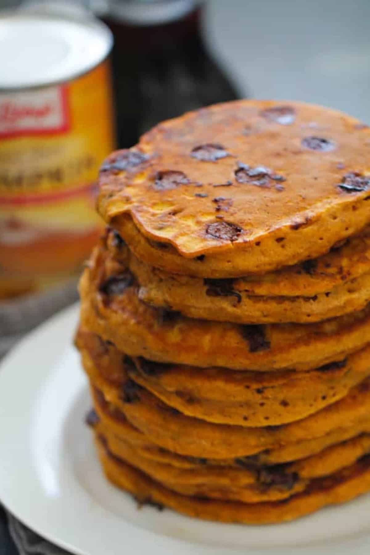 A stack of chocolate chip pancakes is piled on a white plate with a canned product visible in the background.