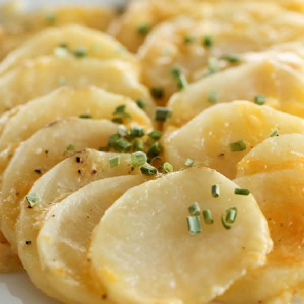 A plate of thinly sliced, cooked potatoes garnished with finely chopped green herbs.