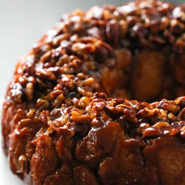 A close-up photo of a sticky, glazed monkey bread covered with chopped pecans on a white plate.