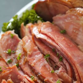 Close-up of slices of glazed ham garnished with fresh parsley, arranged on a white plate.