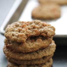 Close-up of a stack of four oatmeal cookies in front of a baking tray with more cookies.