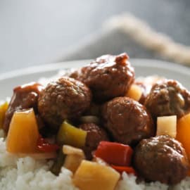 A plate of white rice topped with meatballs and diced vegetables in sauce.