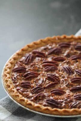 A freshly baked pecan pie with a golden crust on a checkered cloth surface.