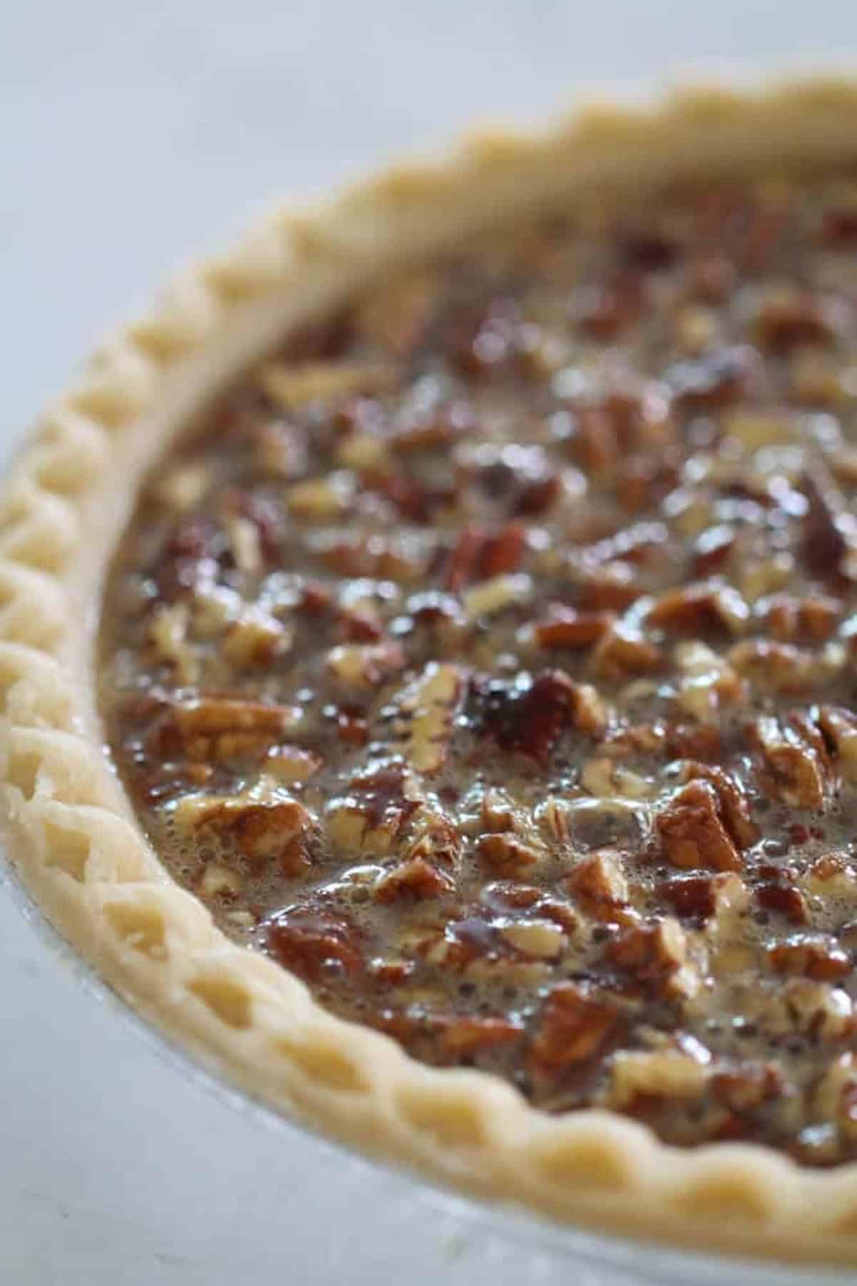 Close-up of an unbaked pecan pie with a crimped crust, filled with a mixture of pecans and filling.