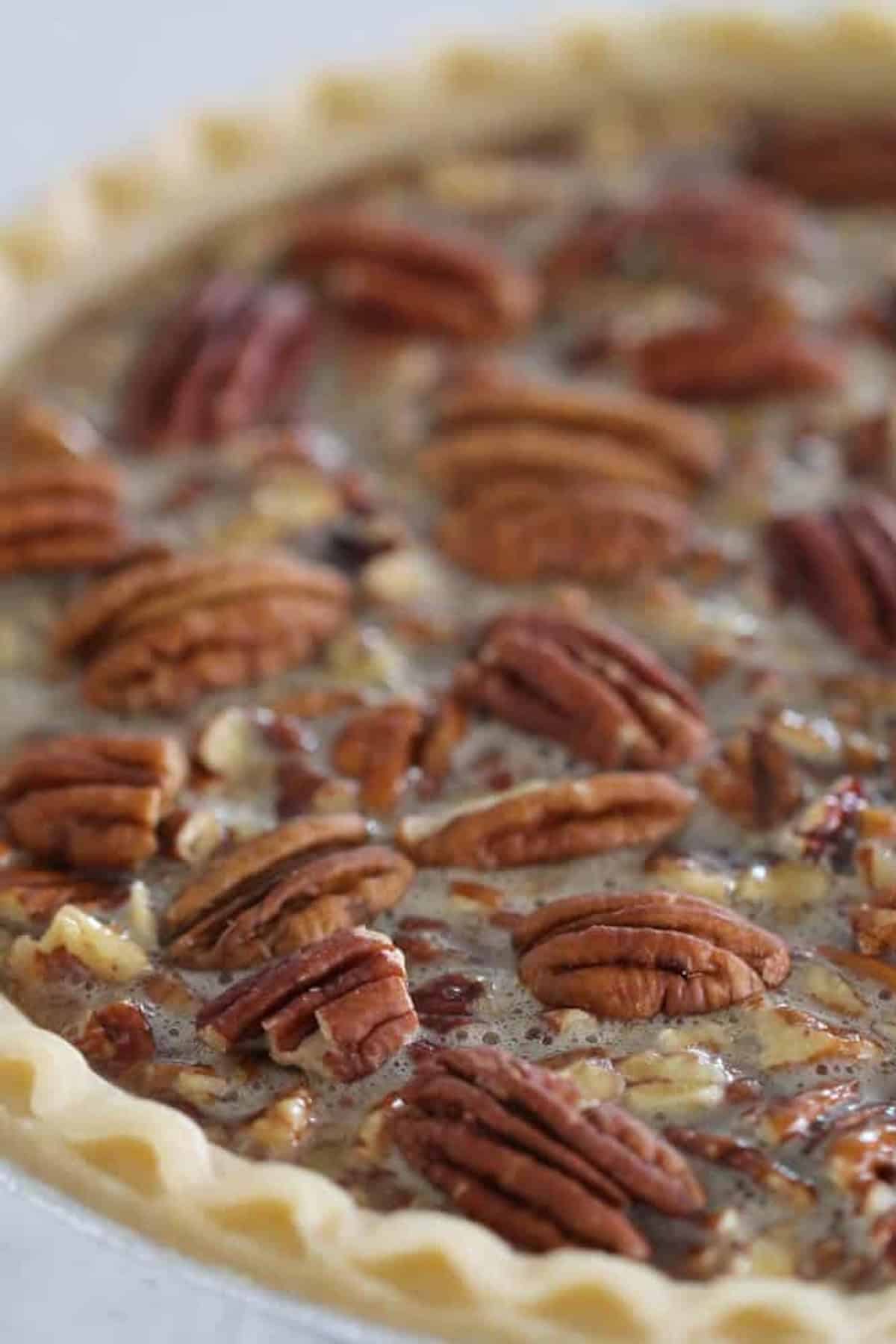 Close-up of a pecan pie with a flaky crust, featuring a layer of whole pecans on top of a caramelized filling.